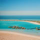Aerial view of overwater bungalows in turquoise Red Sea waters with pristine white sand beach and coastal resort in backgroun