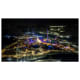 Aerial night view of Qiddiya theme park illuminated with blue and gold lights, featuring roller coasters and carnival attract