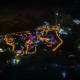 Aerial nighttime view of illuminated theme park with golden and purple lights outlining pathways and attractions against dark