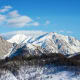 Snow-covered mountains with forested slopes under clear blue sky, winter landscape in Azerbaijan