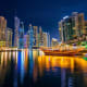 Dubai Marina skyline at night with illuminated skyscrapers and traditional wooden dhow boat on calm water