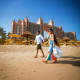 Couple walking on beach with Atlantis The Palm luxury resort hotel in background under clear blue sky