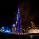 Burj Khalifa illuminated in blue at night with surrounding Dubai skyscrapers and golden-lit buildings in the background