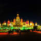 Illuminated Thai Buddhist temple at night with golden spires and colorful green lighting, featuring ornate architecture and d