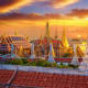 Grand Palace Bangkok at sunset with golden spires and traditional Thai temple architecture illuminated against orange sky