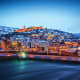 Tbilisi cityscape at dusk with illuminated buildings, Metekhi Church on snowy hillside, and frozen Mtkvari River in foregroun