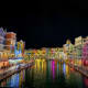 Colorful waterfront buildings reflecting in canal waters at night in Venice-inspired theme park with illuminated architecture