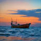 Traditional wooden fishing boat anchored in calm ocean waters during golden sunset with colorful sky
