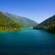 Turquoise alpine lake surrounded by forested mountains under clear blue sky, Himalayan valley landscape