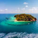 Tropical island surrounded by turquoise water with moored boats and sandy beach, lush green forest covering hilltop
