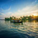 Traditional wooden houseboat on backwaters at sunset with palm trees and clear sky reflecting on calm water