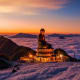 Illuminated golden Buddha statue on mountain peak above sea of clouds at sunset in Sapa, Vietnam