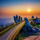 Golden Bridge held by giant blue stone hands at sunset in Da Nang, Vietnam with misty mountains in background