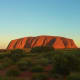Uluru (Ayers Rock) glowing red at sunset in the Australian outback with sparse desert vegetation in foreground