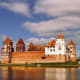 Mir Castle reflected in water, medieval fortress with red-tiled towers and white central keep in Belarus