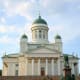 Helsinki Cathedral with white neoclassical facade, green domes, and gold crosses against blue sky with clouds