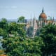 Hungarian Parliament Building with copper dome and Gothic spires viewed through green foliage, Danube River in background