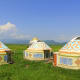 Traditional yurts with ornate blue and orange patterns on green steppe landscape with mountains in Kyrgyzstan