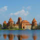 Trakai Island Castle reflected in water, featuring distinctive red-brick towers under blue sky in Lithuania