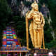 Giant golden statue of Lord Murugan at Batu Caves with colorful rainbow staircase and limestone cliffs in Malaysia