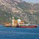 Kotor Bay coastal landscape with historic mosque featuring white dome and minaret, red and white passenger ferry boat, limest