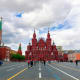 Red Square in Moscow with State Historical Museum and Kremlin tower under cloudy sky, tourists walking on brick plaza