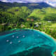Aerial view of a turquoise bay with sailboats, white sand beach, and lush forested mountains in Seychelles