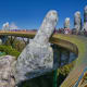 Giant stone hands supporting a curved bridge with tourists walking across, Golden Bridge in Da Nang, Vietnam