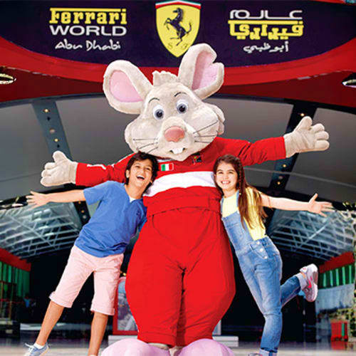 Two children posing with a large pink mouse mascot character at Ferrari World Abu Dhabi theme park entrance