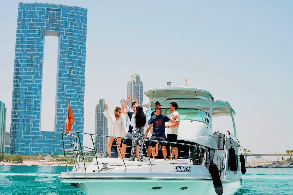 Group of tourists on a white yacht in turquoise waters with Dubai's Frame landmark and high-rise buildings in the background
