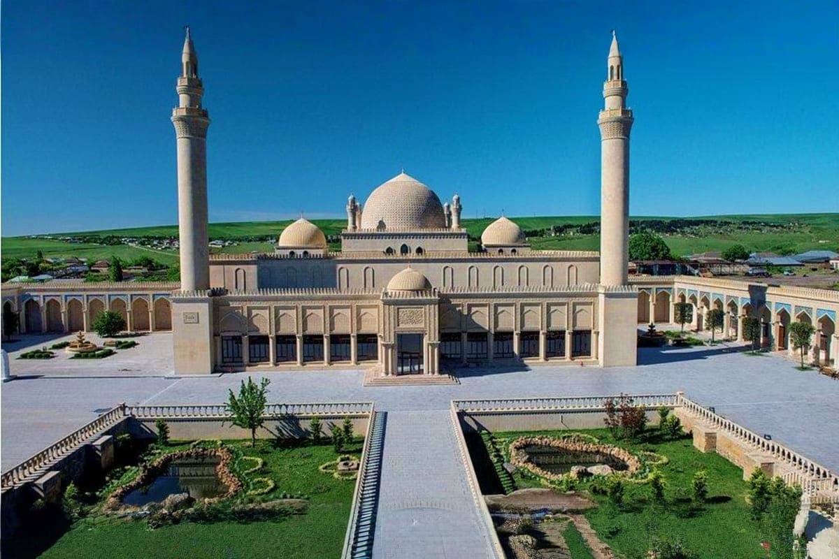 Historic mosque in Gabala with two tall minarets, central dome, and manicured courtyard gardens under clear blue sky