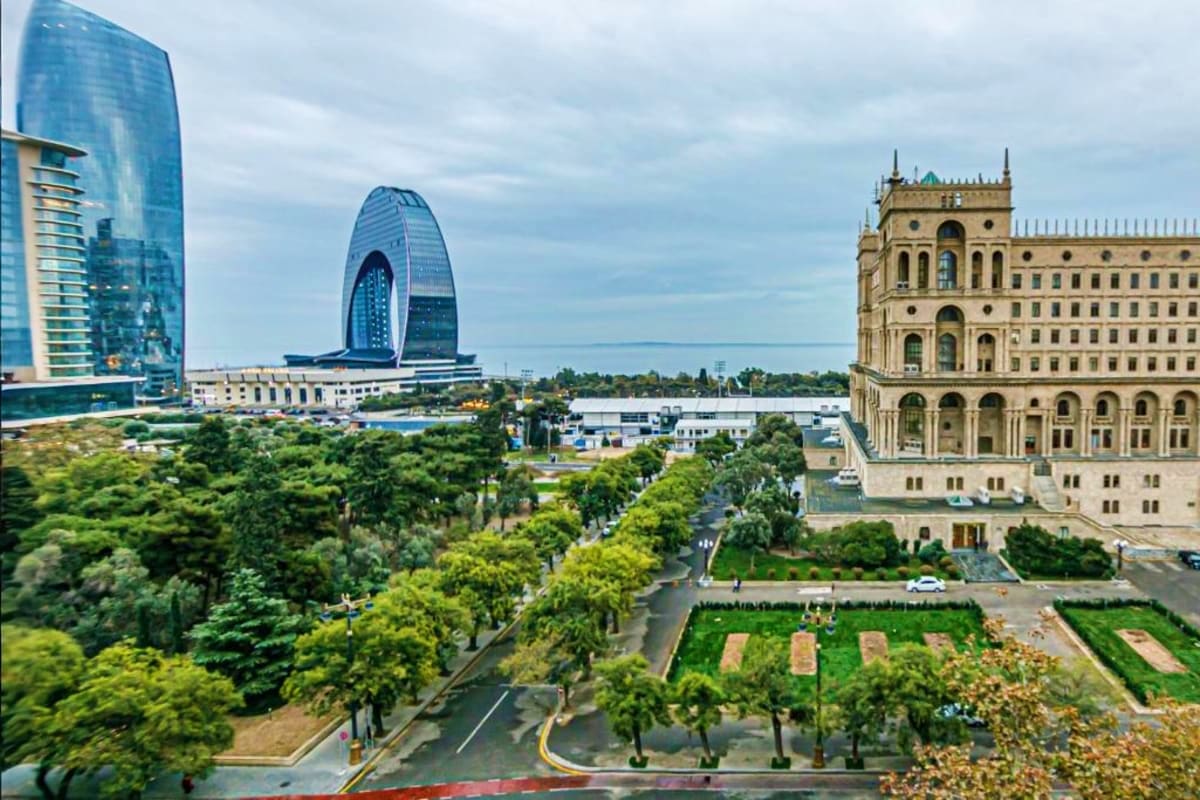 Baku cityscape showing modern blue glass buildings and historic Government House with green park and trees in foreground
