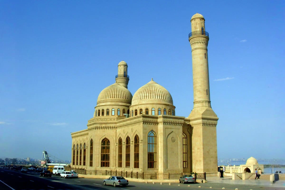Heydar Aliyev Mosque in Baku with beige stone facade, dual domes, minaret, and Caspian Sea waterfront
