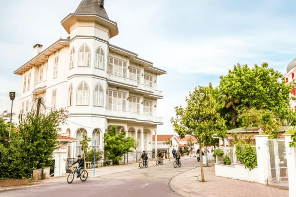 Historic white tower building with spire on pedestrian street, cyclists riding bikes, green trees and white buildings in back