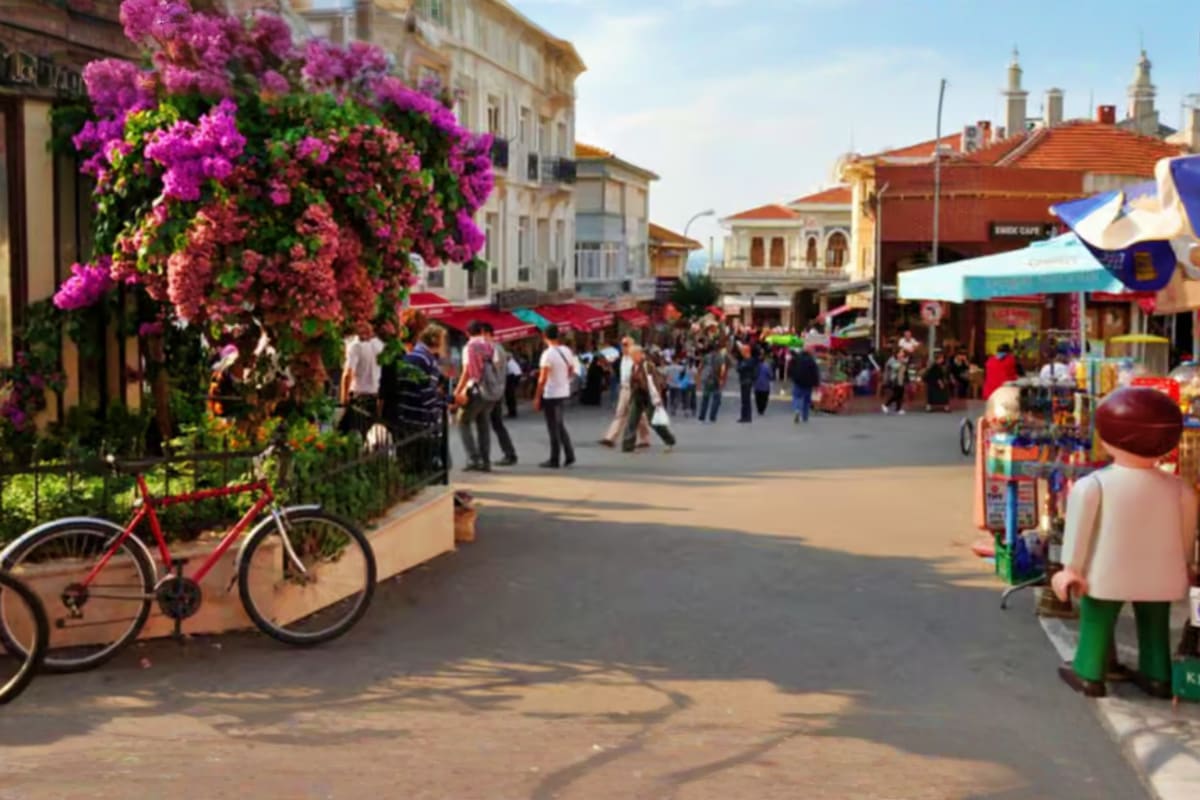 Colorful European town square with pink bougainvillea flowers, red bicycle, historic buildings, and tourists shopping at mark