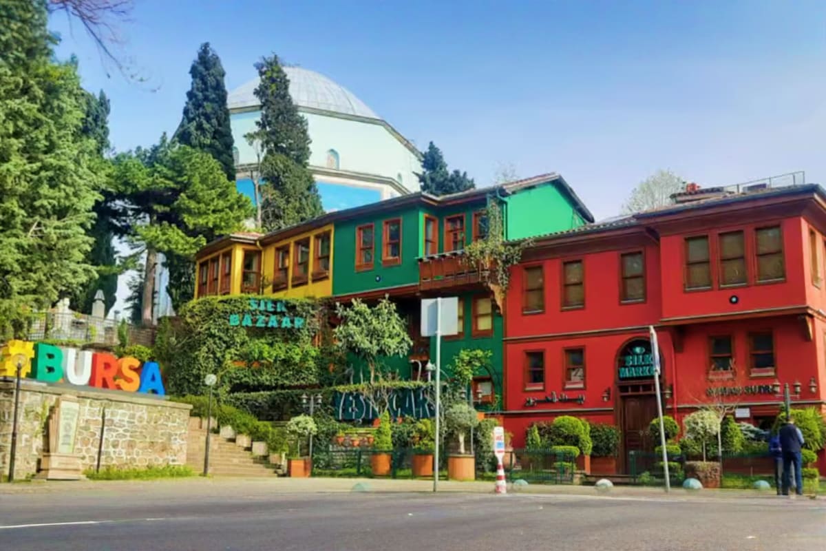 Colorful historic buildings in Bursa's Bazaar district with green cypress trees and dome structure in background