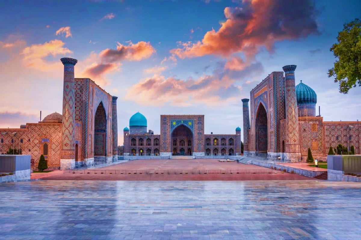 Registan Square in Samarkand at sunset with three ornate madrasahs featuring turquoise domes and decorated facades under a co