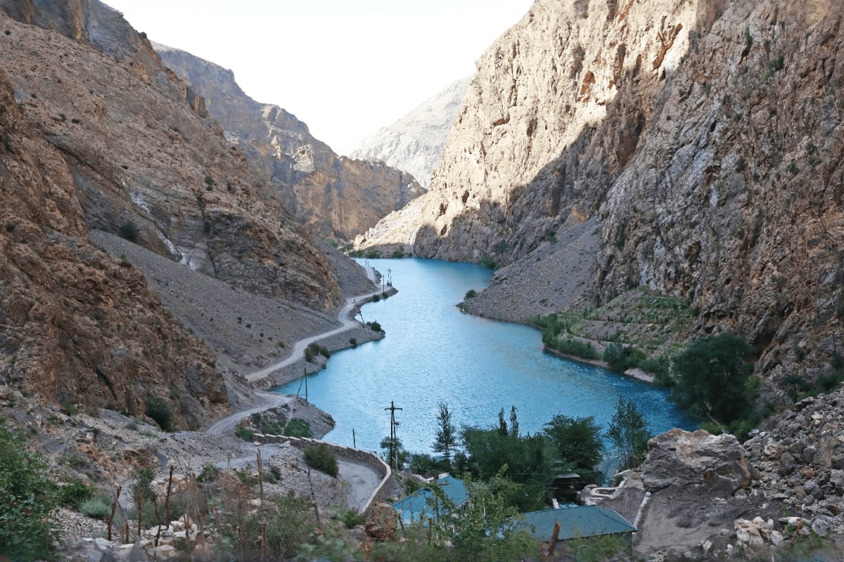 Turquoise mountain lake surrounded by steep limestone cliffs and winding road in Tajikistan's alpine canyon landscape