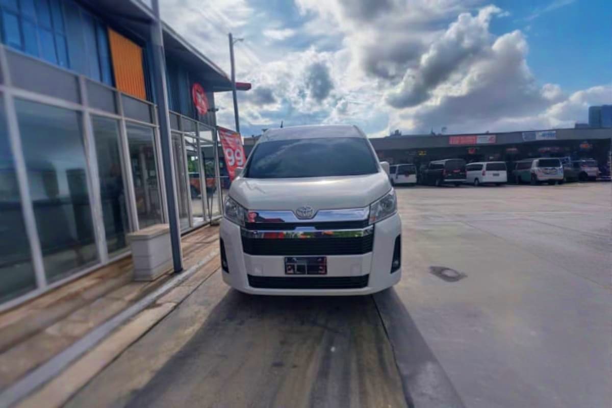 White Toyota minivan parked at dealership entrance with cloudy sky, used for intercity transfer service
