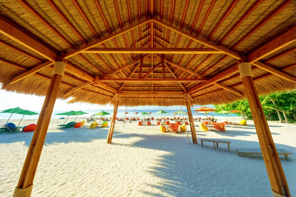 Wooden pavilion with thatched roof on sandy beach with colorful umbrellas and loungers overlooking the ocean