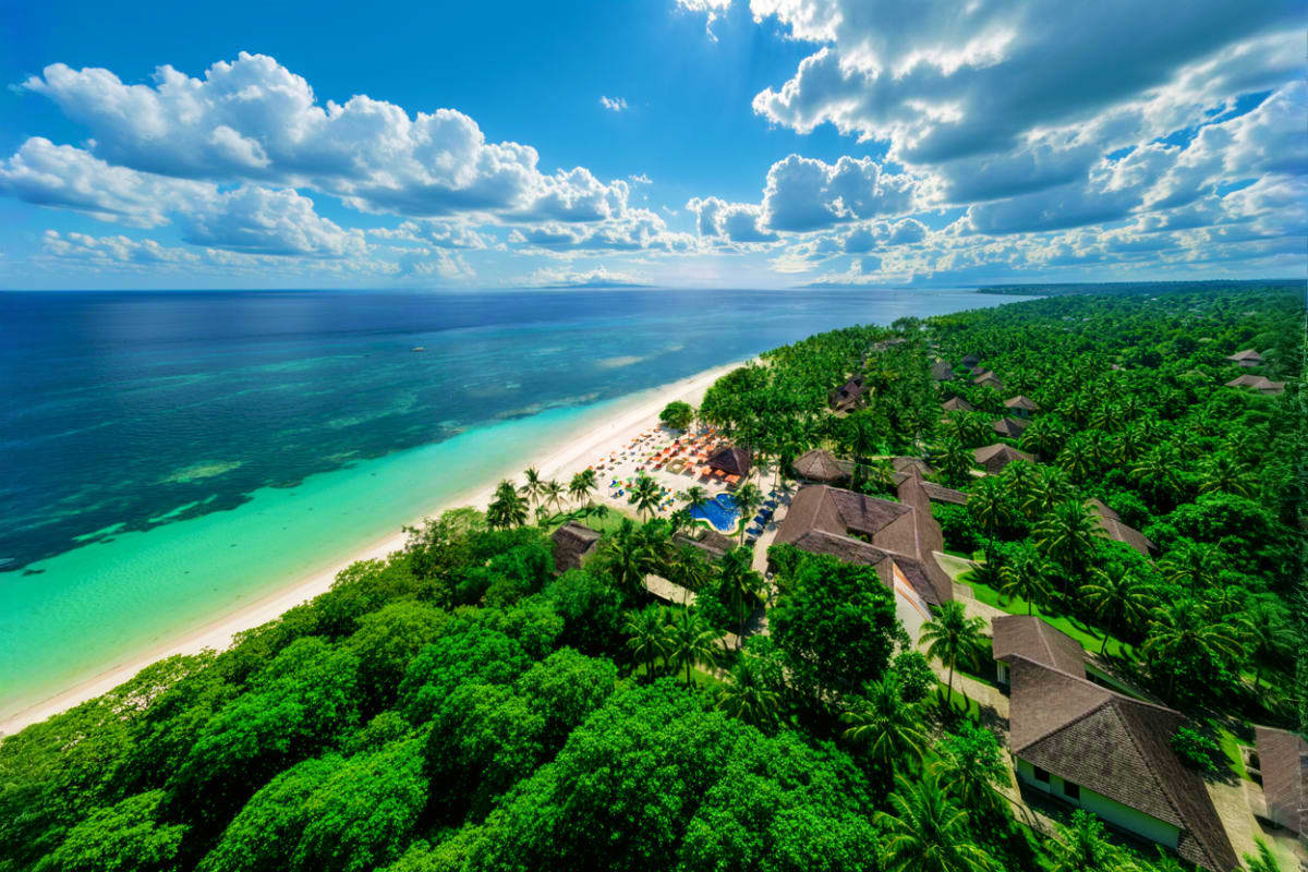 Aerial view of Oceanica Resort Panglao with beachfront bungalows, white sand beach, turquoise ocean, tropical jungle, and blu