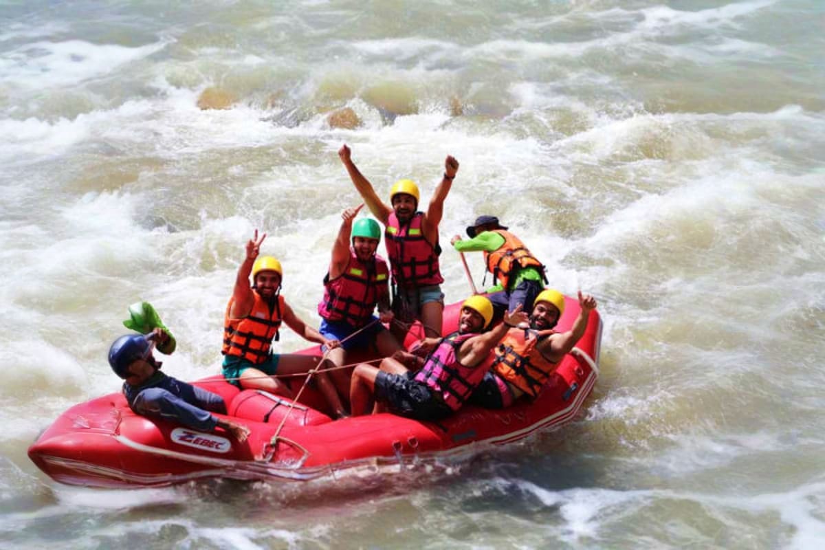Group of people white water rafting in red inflatable boat navigating through turbulent whitewater rapids with paddles.