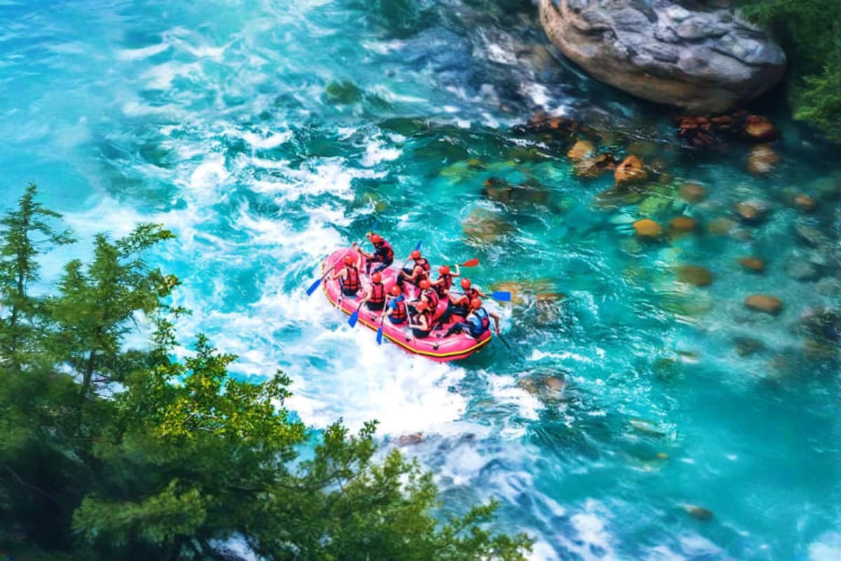 Group of people white water rafting in red inflatable raft on turquoise river with rocky cliffs and trees