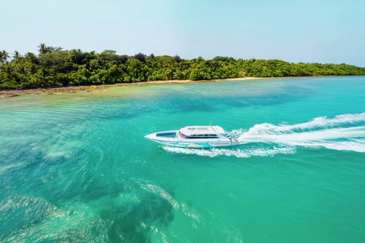 White speed boat riding waves in turquoise tropical waters with lush green coastline and sandy beach in background