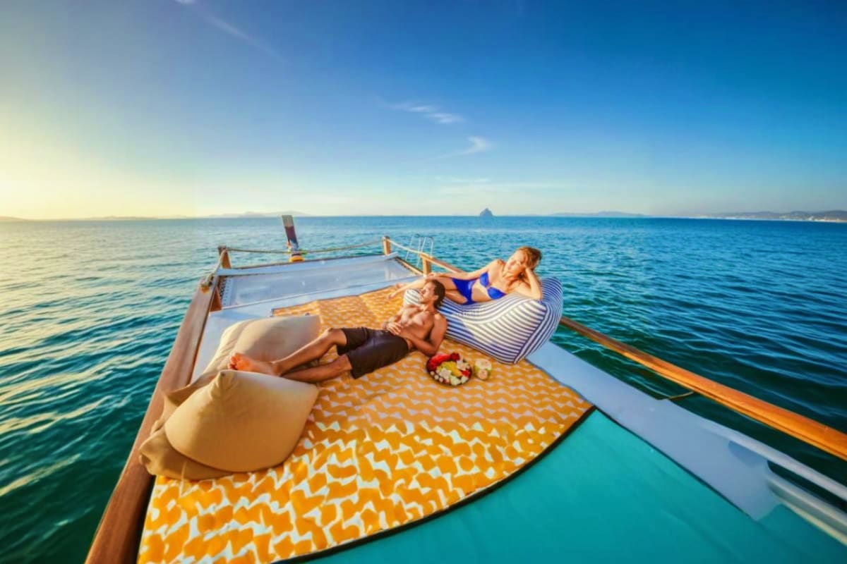 Couple relaxing on colorful cushions aboard a traditional longtail speedboat in turquoise tropical waters during a seven isla