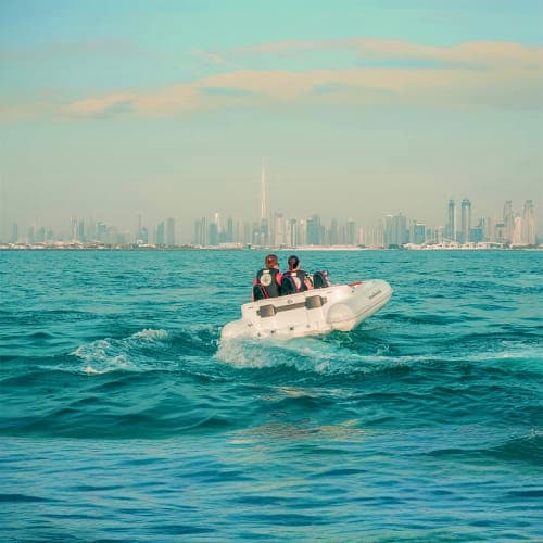 Group of people in white inflatable boat on turquoise water with Dubai skyline and Burj Khalifa in background