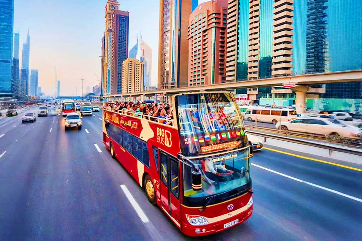 Big Bus Tour Dubai Red double-decker hop-on hop-off tour bus with passengers driving on Dubai highway with modern skyscrapers in background