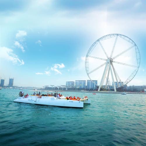 White boat with passengers on turquoise water near giant white Ferris wheel and Dubai skyline under blue sky