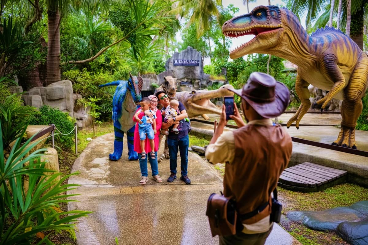 Family posing with dinosaur sculptures at Crocodile Adventureland theme park in Langkawi surrounded by tropical vegetation