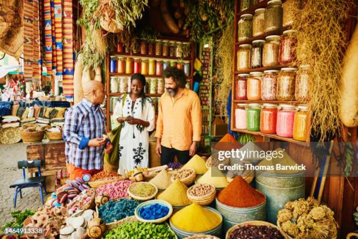 Spice merchant shop in Dubai with colorful powdered spices in bowls, tourists shopping, and shelves of traditional ingredient